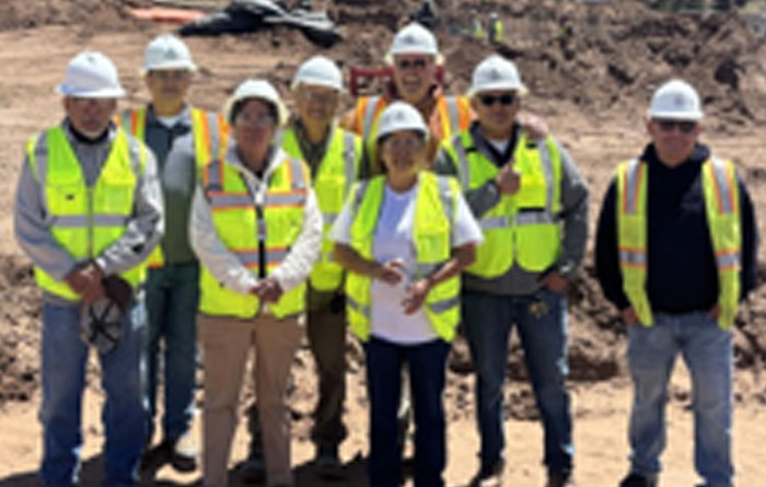 School staff posing outside in wearing construction hats and yellow protected vests