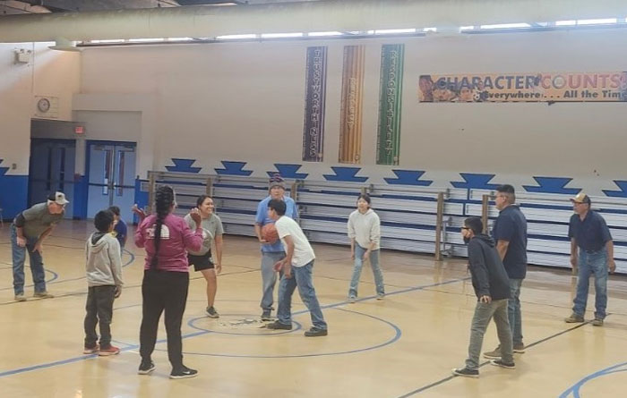 Alt text: Staff and students gather at center court in a school gymnasium during a friendly basketball game at Crystal Boarding School.