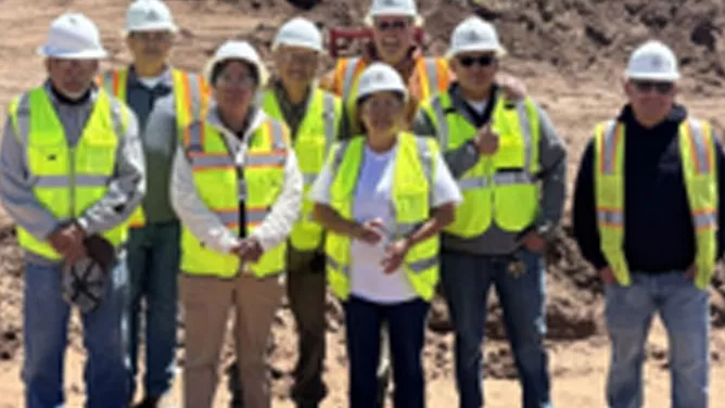 School staff posing outside in wearing construction hats and yellow protected vests