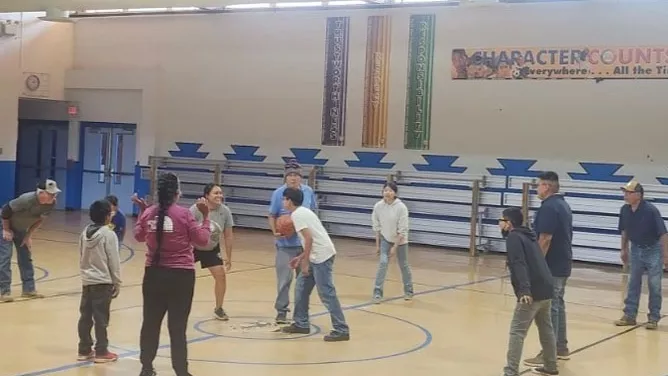 Staff and students gather at center court in a school gymnasium during a friendly basketball game at Crystal Boarding School.